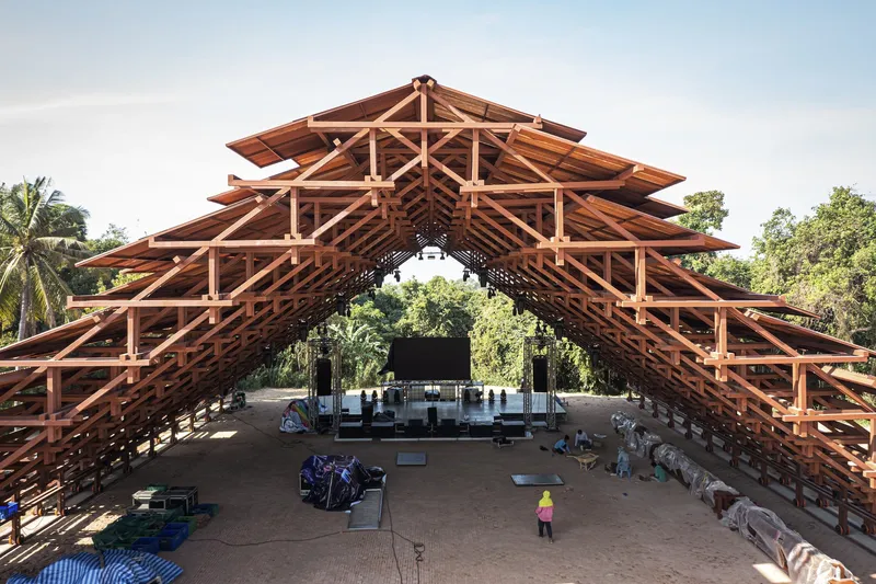 Interior view of the exposed timber truss roof structure with a person on the earthen floor
