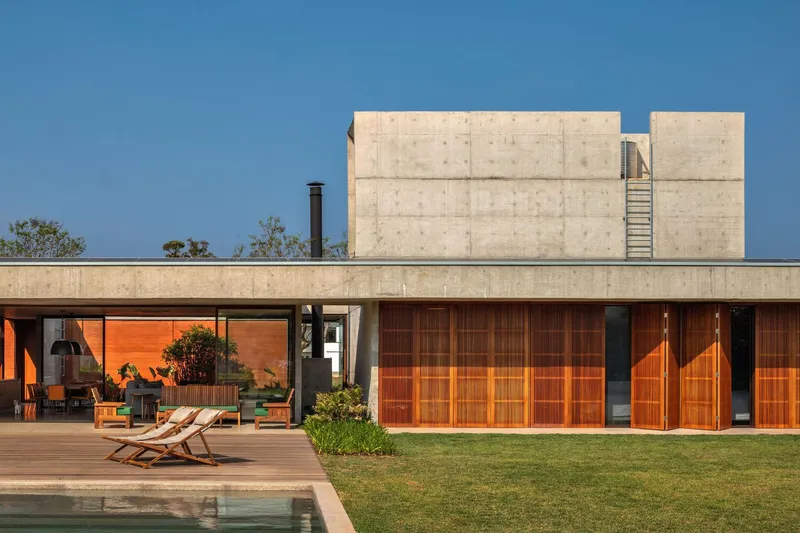 Poolside elevation with horizontal timber shutters and board-formed concrete tower under clear sky