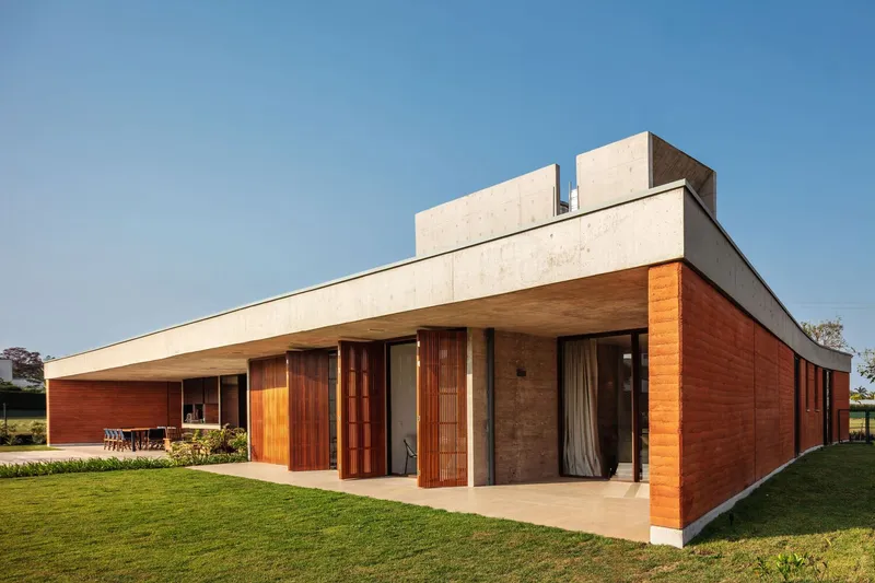 Corner view of the terracotta and timber facade beneath the cantilevered concrete overhang at dusk
