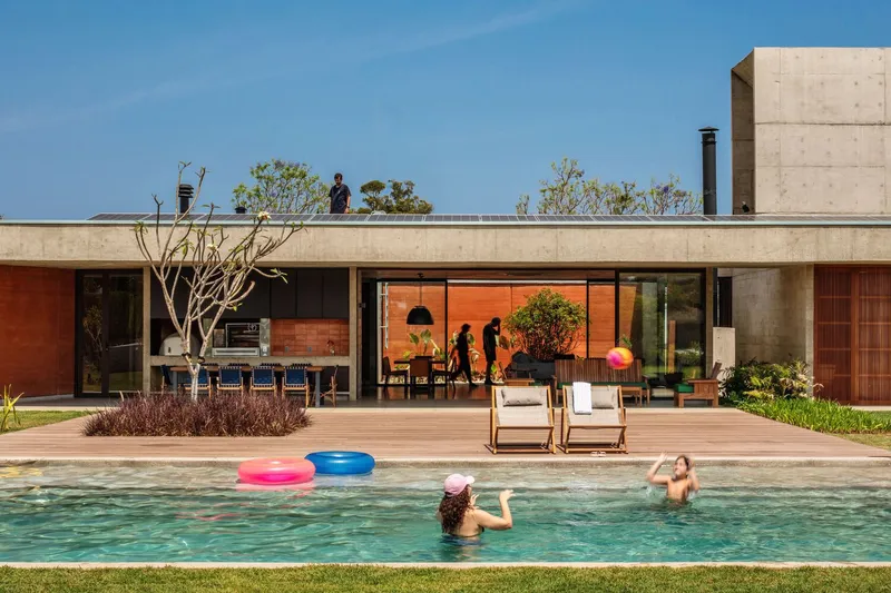 Pool deck with swimmers and families as the glazed living space opens to the lawn