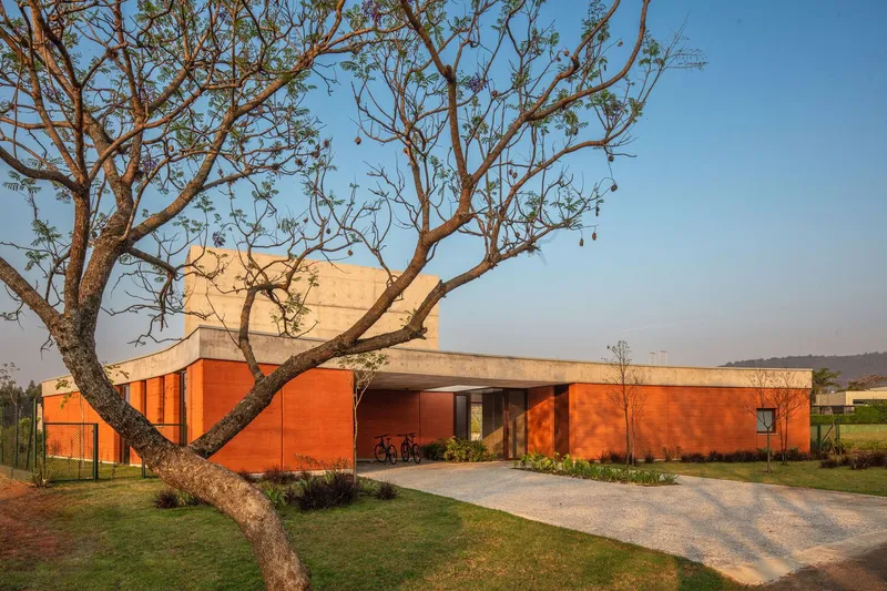 Orange masonry facade with concrete roof overhang framed by a leafless tree in late afternoon light