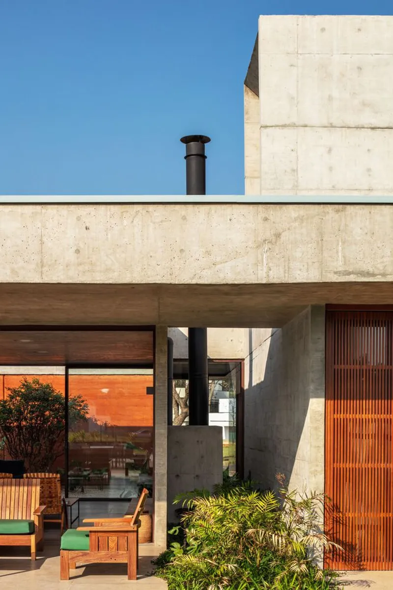 Covered patio with exposed concrete beams and timber slatted screens beside planted beds under midday sun