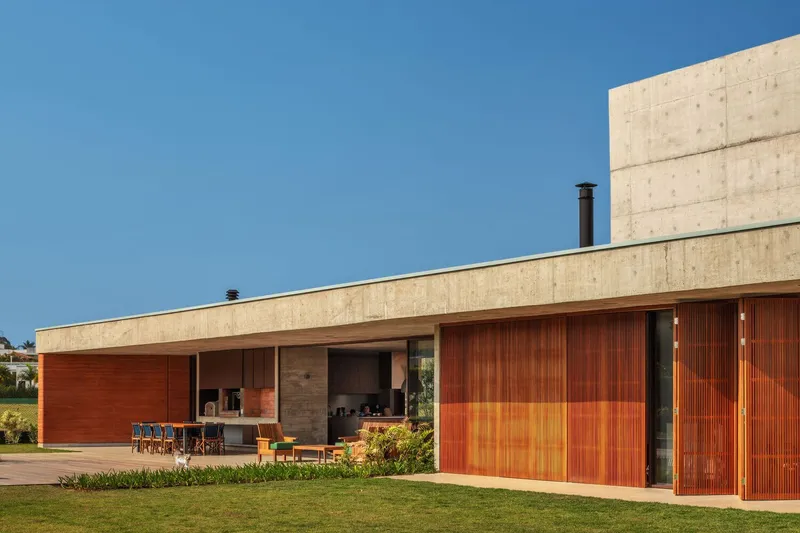 Rear elevation showing timber louvered panels and outdoor kitchen beneath concrete soffit at dusk