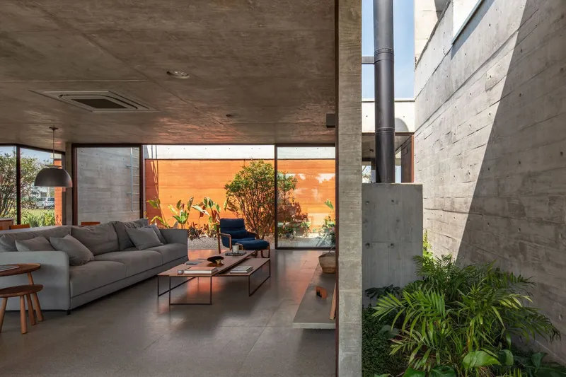 Interior living room with board-formed concrete walls and glazed courtyard opening containing planted greenery
