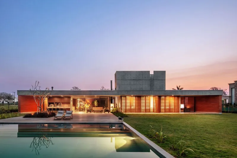 Garden view of the elongated wood-clad facade with glazed openings and concrete tower at dusk