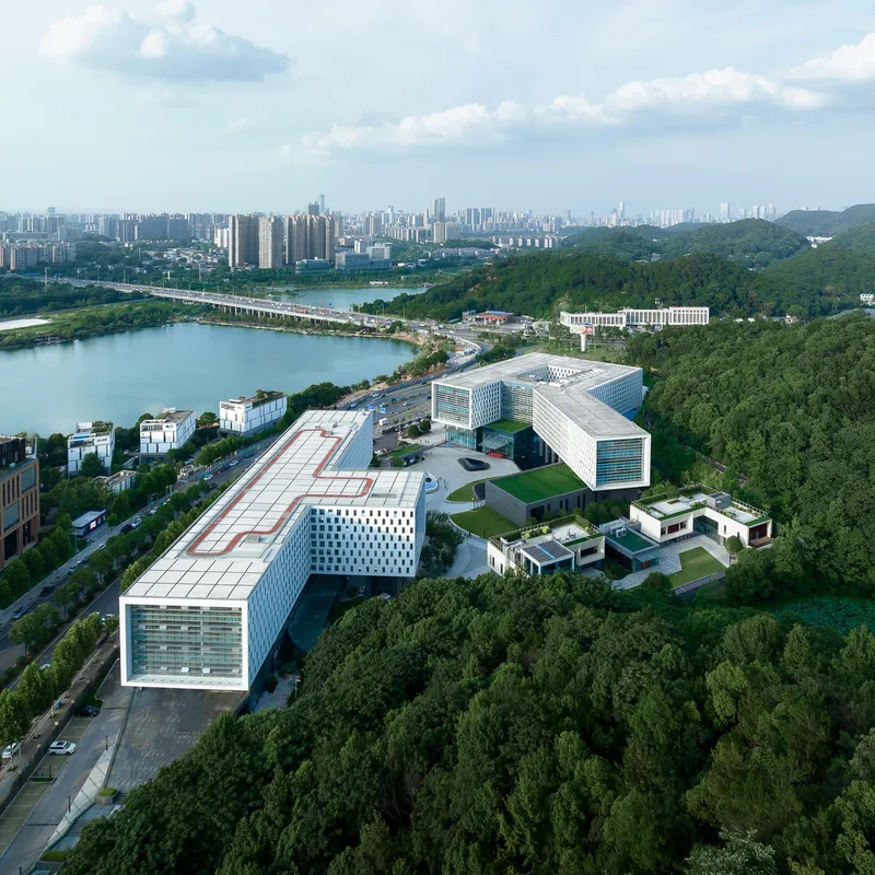 Aerial view of the campus complex with white perforated facades nestled among forested hills and a lake