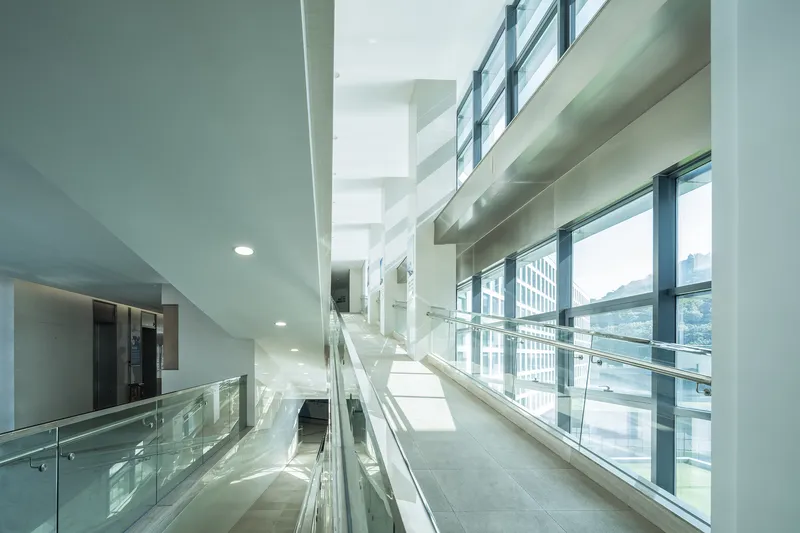 Interior corridor with glass balustrade and full-height windows overlooking the courtyard in bright daylight