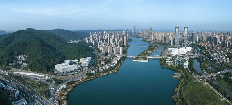 Wide aerial panorama showing the campus buildings positioned between the river and green mountain slopes