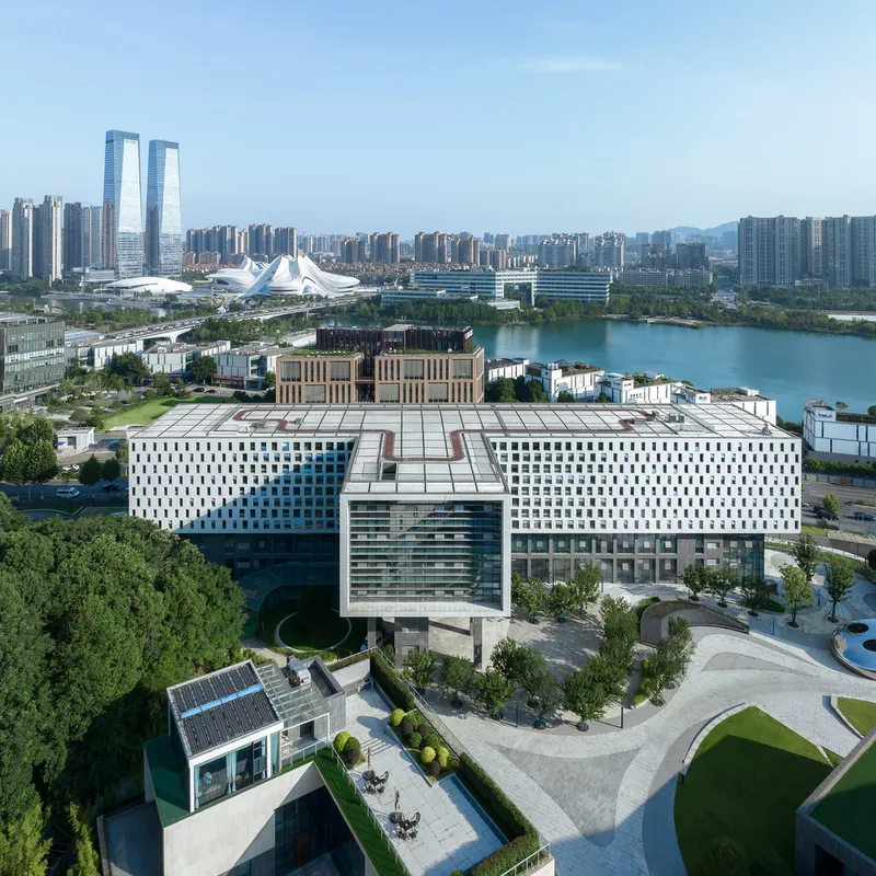 Aerial view of the perforated white facades forming a T-shaped plan with landscaped courtyard and lake beyond