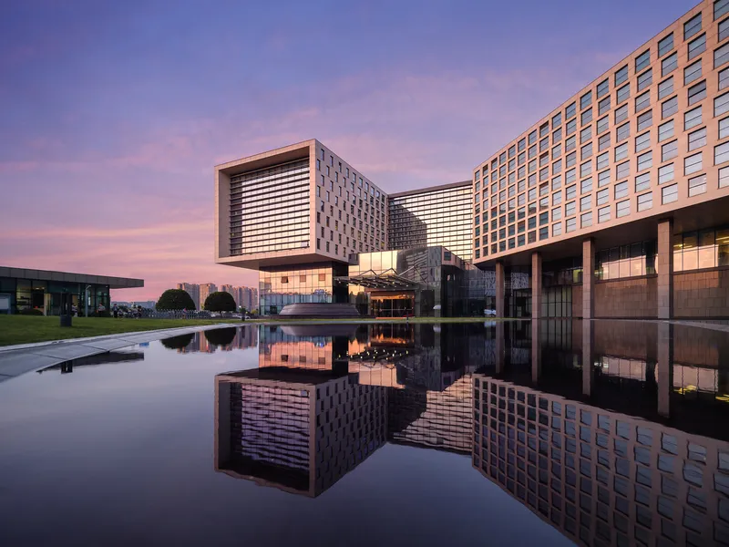 Reflecting pool mirroring the cantilevered volumes and patterned facades at dusk with pink sky