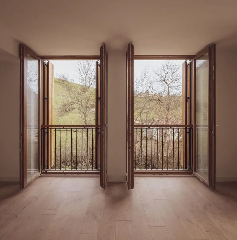 Twin French doors with metal balconies opening to bare winter hillside with leafless trees