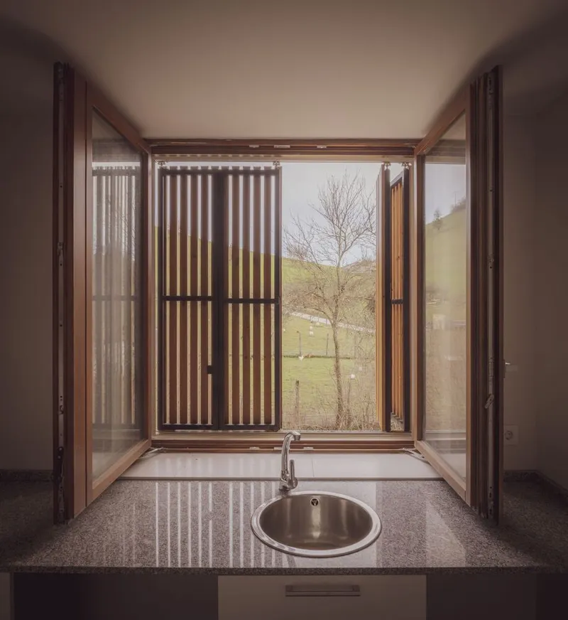 Interior window bay with timber frame and vertical screen opening to hillside with bare tree