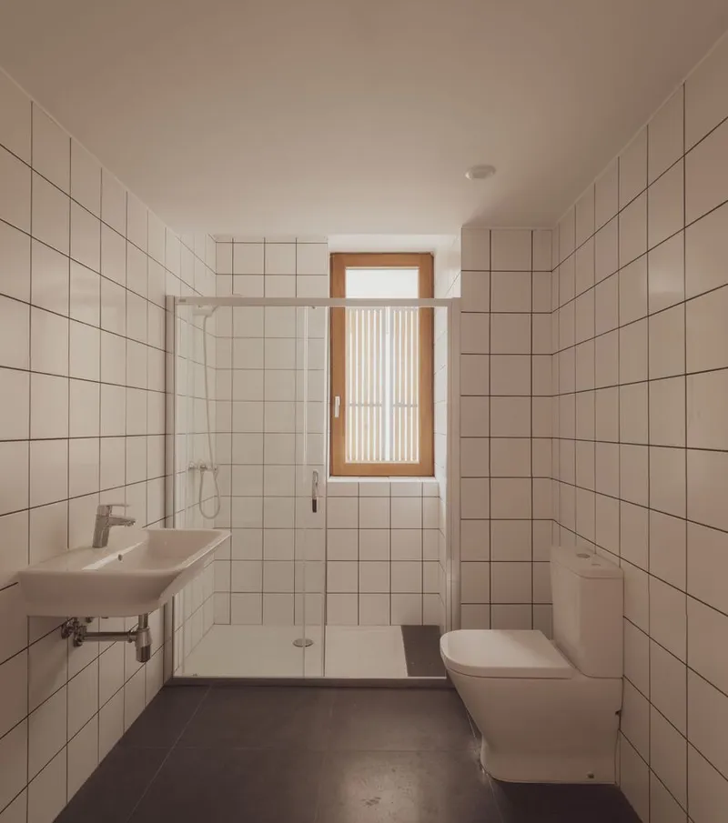 White tiled bathroom with glass shower partition and timber-framed window with vertical slat screen