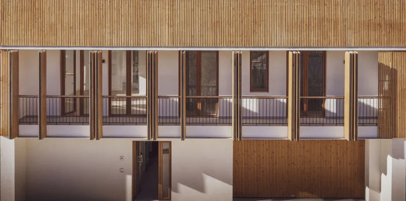 Interior corridor with vertical timber shutters across glass balconies under slatted timber soffit at twilight