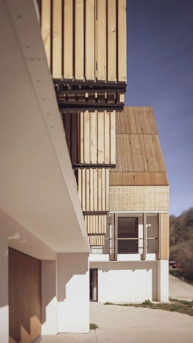 Exterior view showing vertical timber slat facade and dark metal balcony railings under blue sky