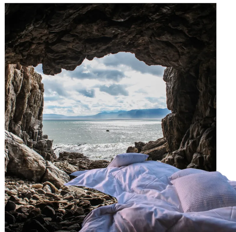View from inside a coastal cave with white bedding on pebbles framing the ocean and distant mountains