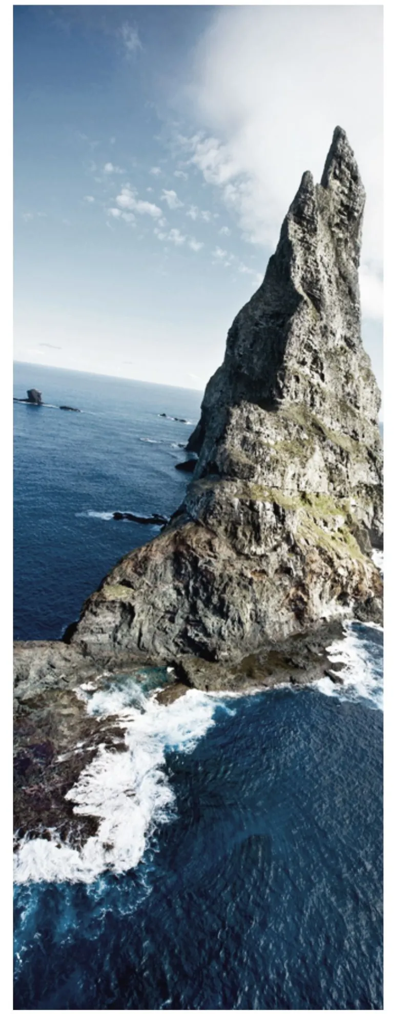 Tall jagged sea stack rising from blue ocean waters under a clear sky