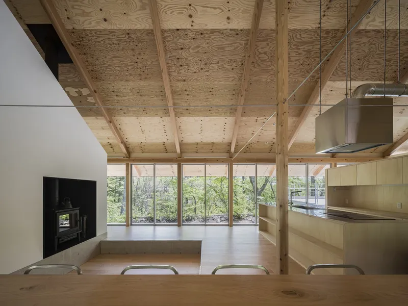 Dining area with plywood ceiling and timber columns framing views to the forested exterior