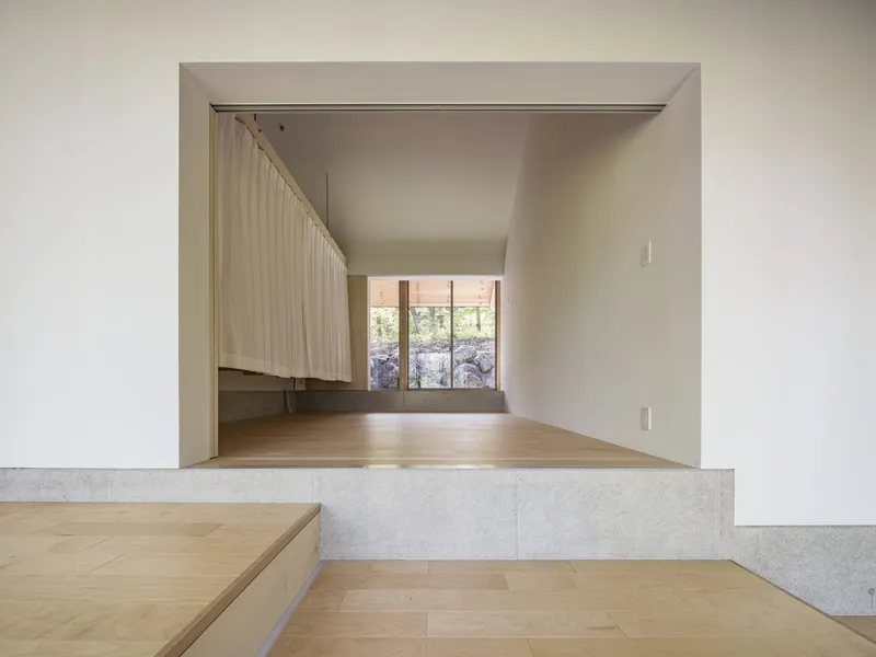 Split-level interior with concrete and timber platforms framing a view through doorway to distant window