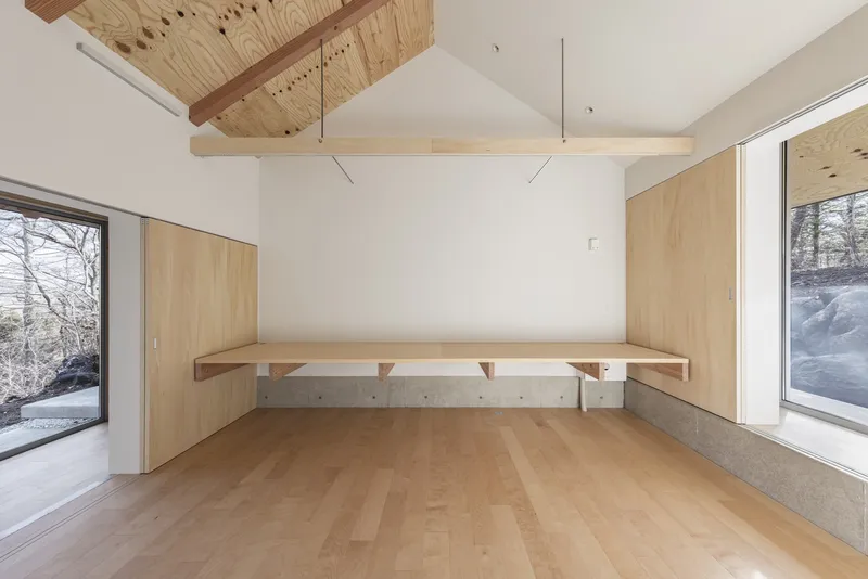 Room with timber-lined walls, concrete bench seating below windows, and exposed plywood ceiling above white partition