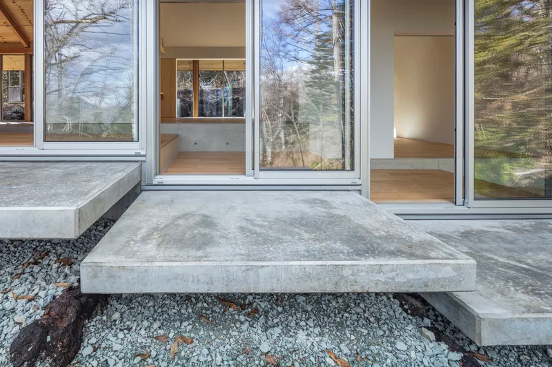 Concrete step platforms set in crushed stone leading to glazed doorways under bare trees