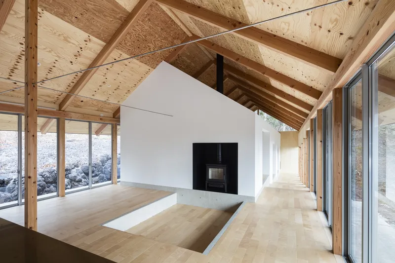 Interior with exposed timber roof trusses, white gabled volume with black fireplace, and sunken seating area