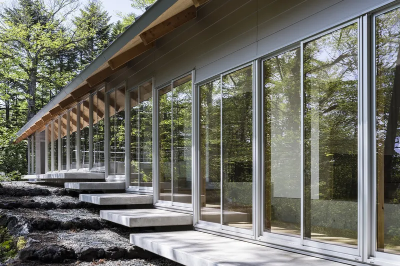 Exterior corridor with concrete pads stepping across black volcanic rock under a deep timber soffit