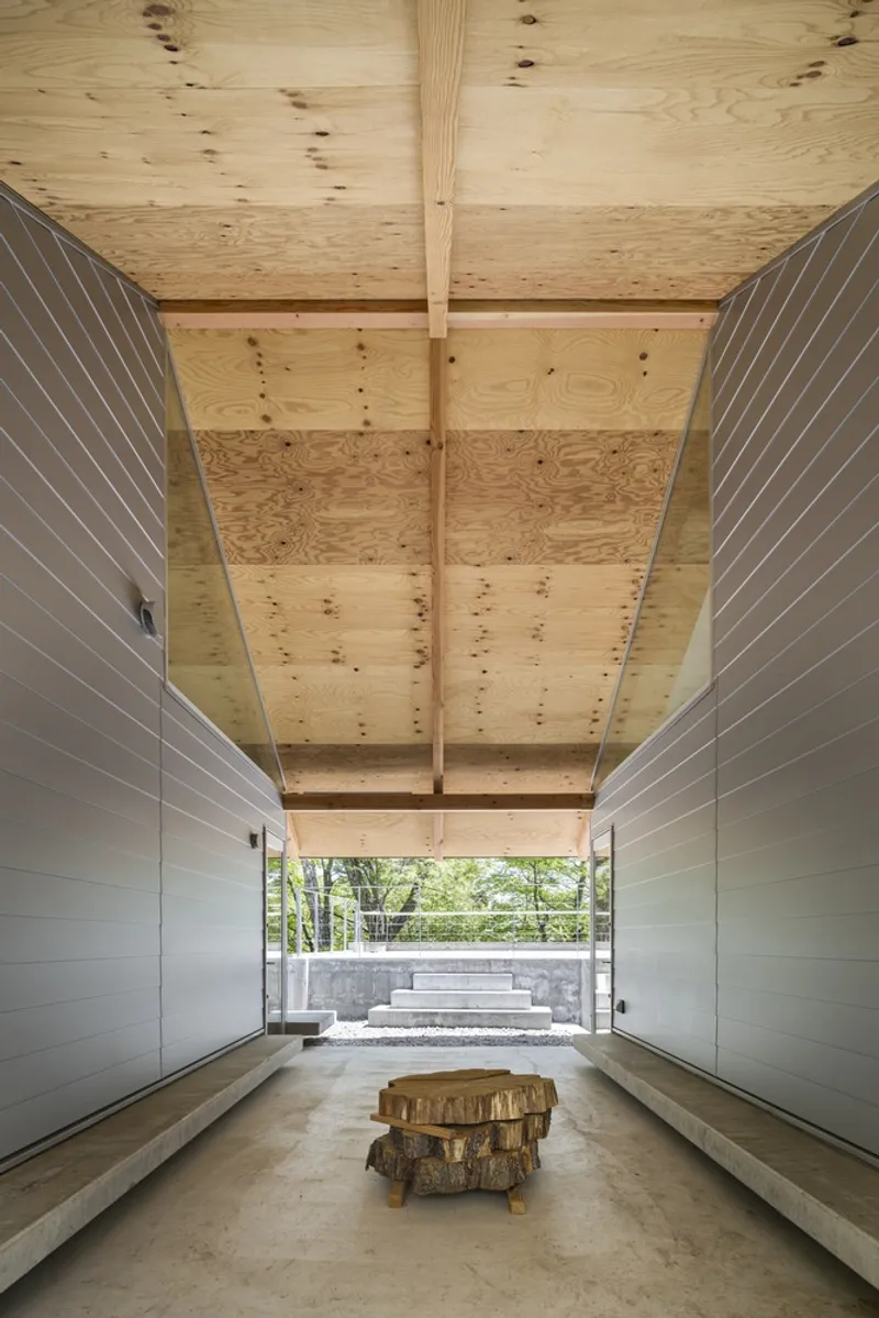 Corridor with timber-clad ceiling, horizontal slatted side walls, and tree-stump furniture beneath clerestory opening