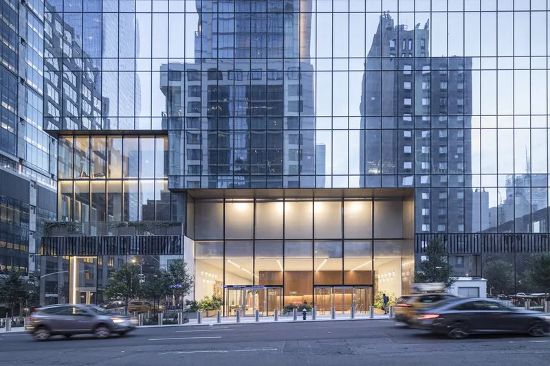 Two-story glass lobby entrance at street level with cars passing by at dusk