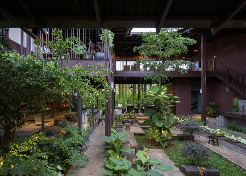 Internal courtyard with timber columns, exposed ceiling beams, and planted beds with tropical vegetation under diffuse daylight
