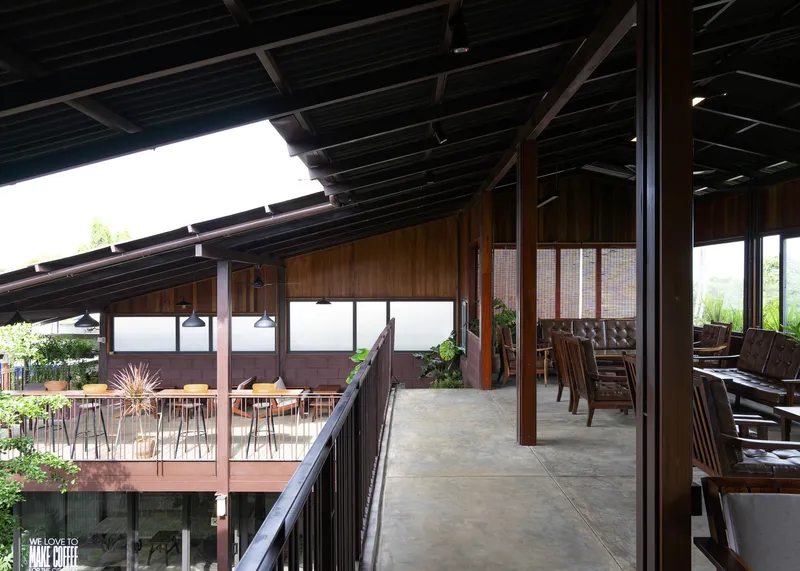 Covered walkway with steel columns and timber ceiling joists overlooking a terrace with outdoor seating