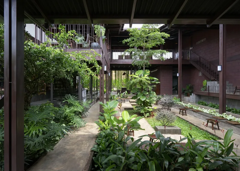 Sheltered courtyard with timber post-and-beam structure, winding paths through planted garden beds, and upper-level balconies