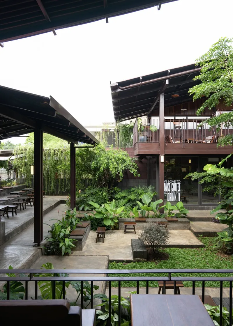 View across the planted courtyard showing two covered pavilions with pitched roofs and timber columns under overcast skies