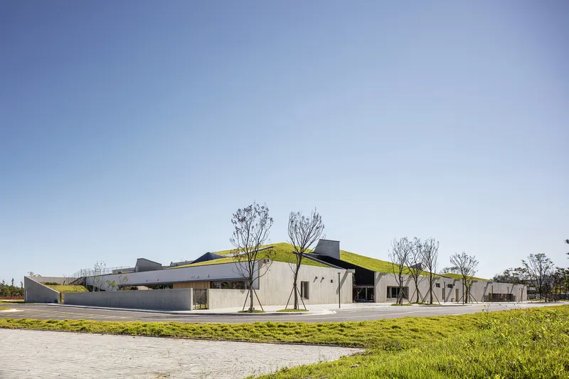 Corner view of the grass-covered undulating roof with young trees planted along the paved perimeter