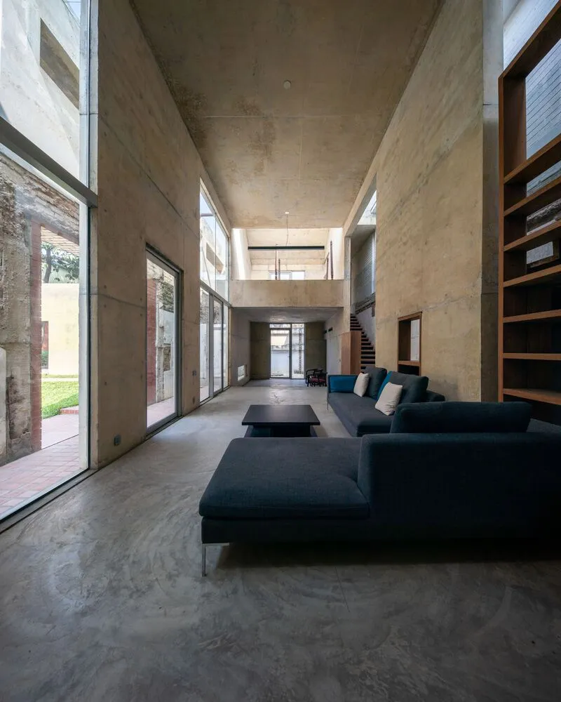 Living space with board-formed concrete walls and ceiling, timber shelving, and mezzanine level above polished floor