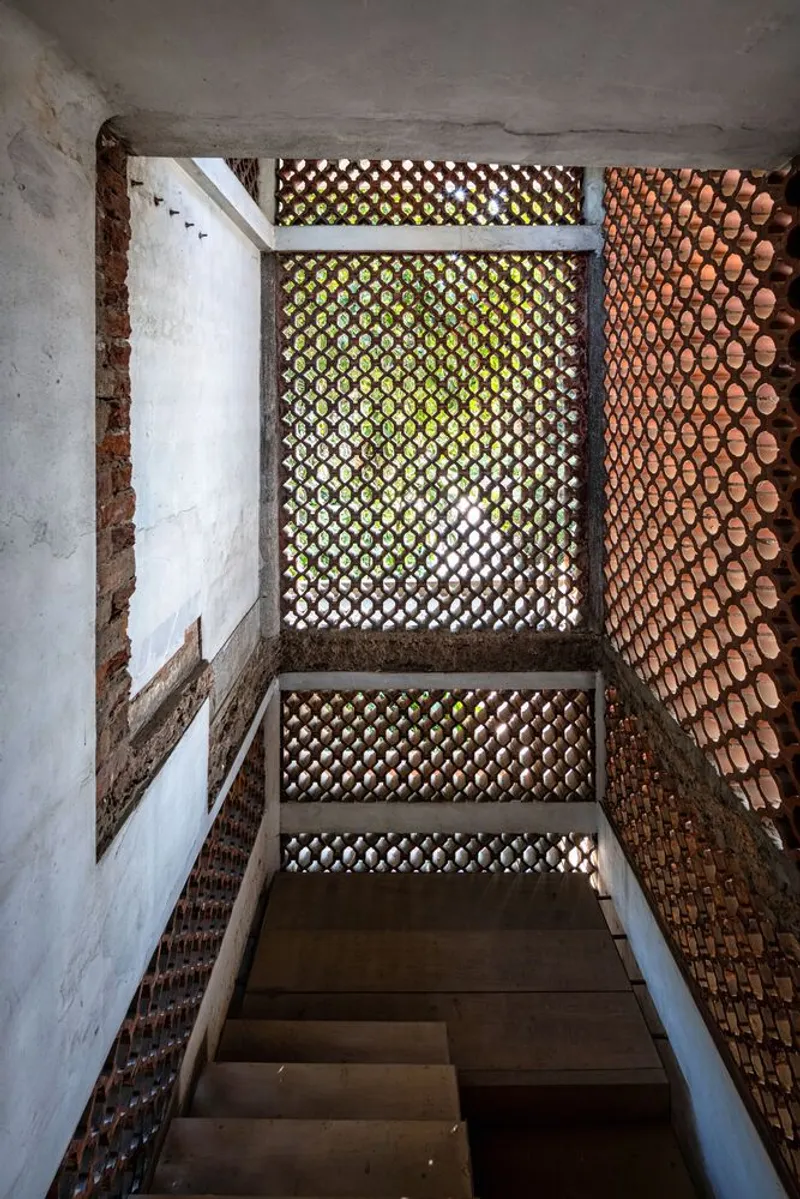 Upward view of perforated brick screen surrounding a timber stair framed by whitewashed walls