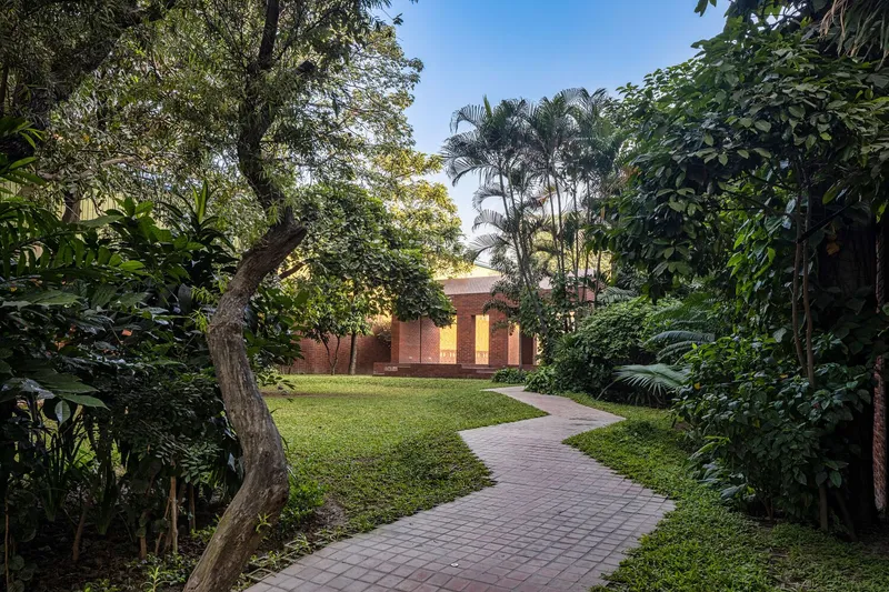 Brick paver pathway winding through lawn and palms toward a red brick pavilion in late afternoon light