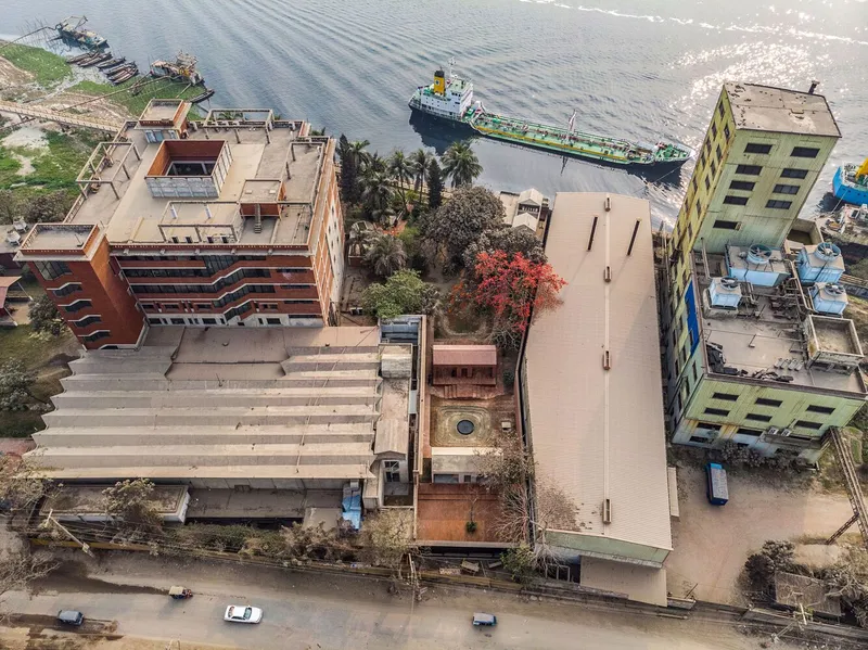 Aerial view of riverside property with terraced concrete roofs, a tanker passing, and adjacent mixed structures