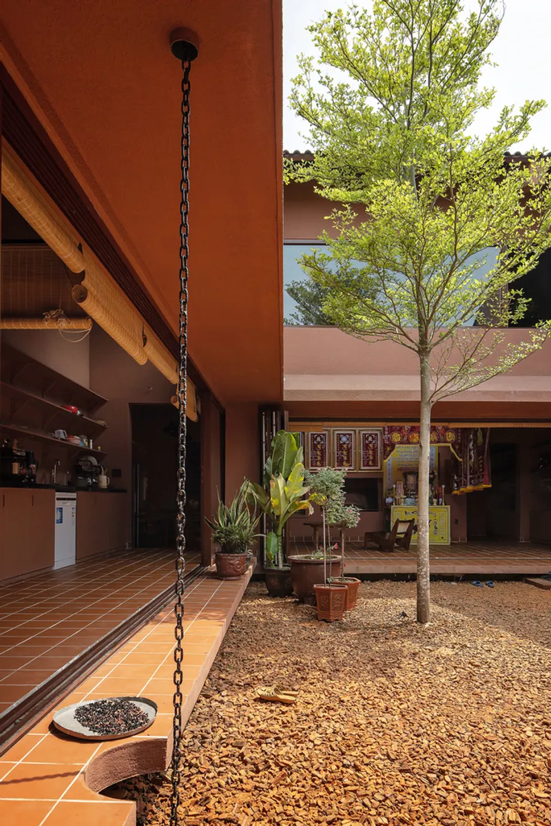 Central courtyard with gravel ground, young tree, and terracotta-tiled covered walkway under morning sunlight
