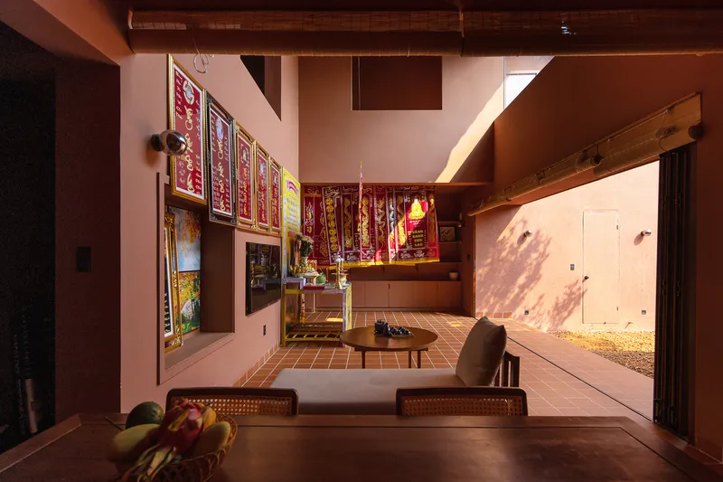 Living area with low seating platform, religious altar, and opening to sunlit courtyard garden