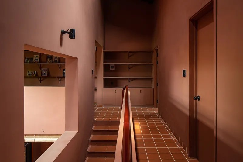 Upper hallway with terracotta tile floor, timber handrail, and built-in storage under soft evening light