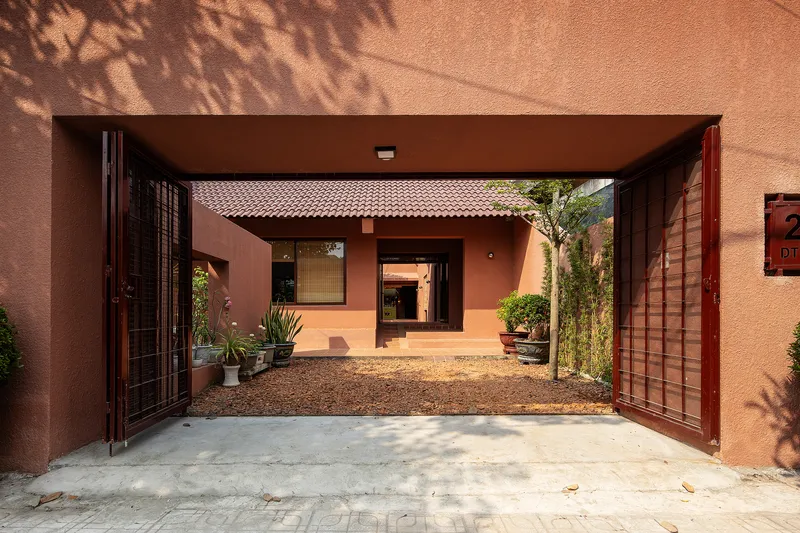 View through open timber gate to interior courtyard with gravel surface and dappled tree shadows