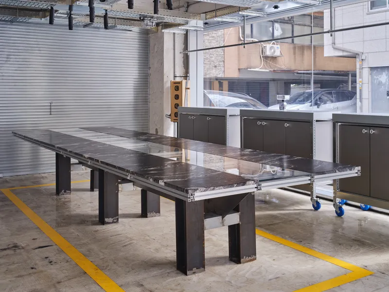 Industrial workshop space with steel work tables and dark metal cabinets beneath corrugated metal cladding