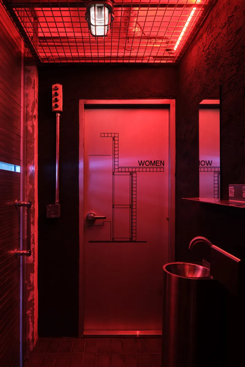 Restroom entrance illuminated by red LED lighting beneath a gridded ceiling panel