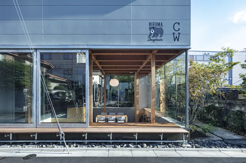 Street view of the raised timber pavilion with full-height glazing and gravel bed at ground level
