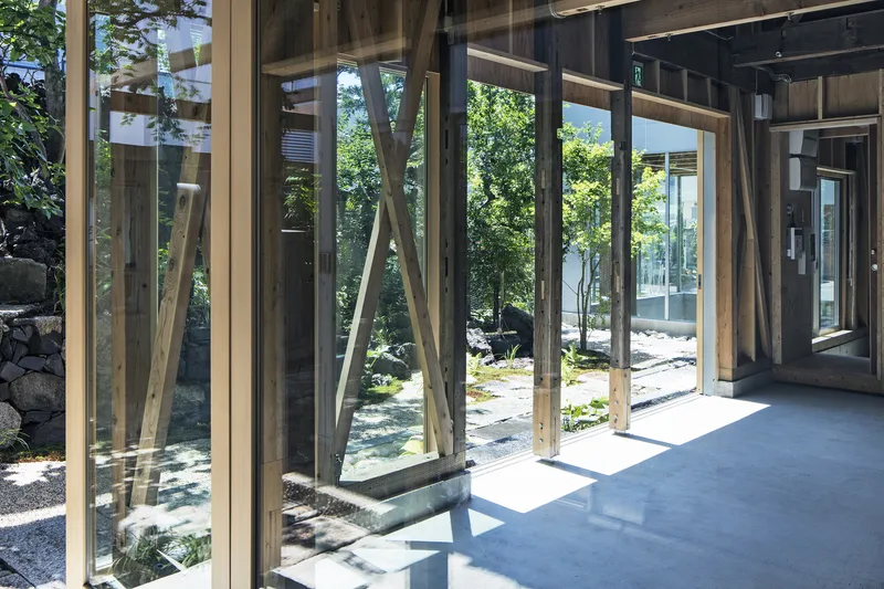 Glass walls with exposed timber framing opening onto a gravel courtyard with stepping stones