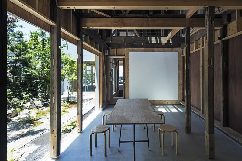 Interior view of timber frame structure with table and stools beneath exposed rafters and beams