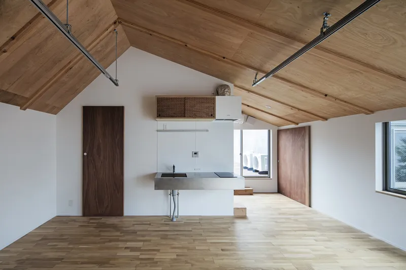 Open interior with plywood vaulted ceiling, wall-mounted sink and dark timber doors under exposed steel beams