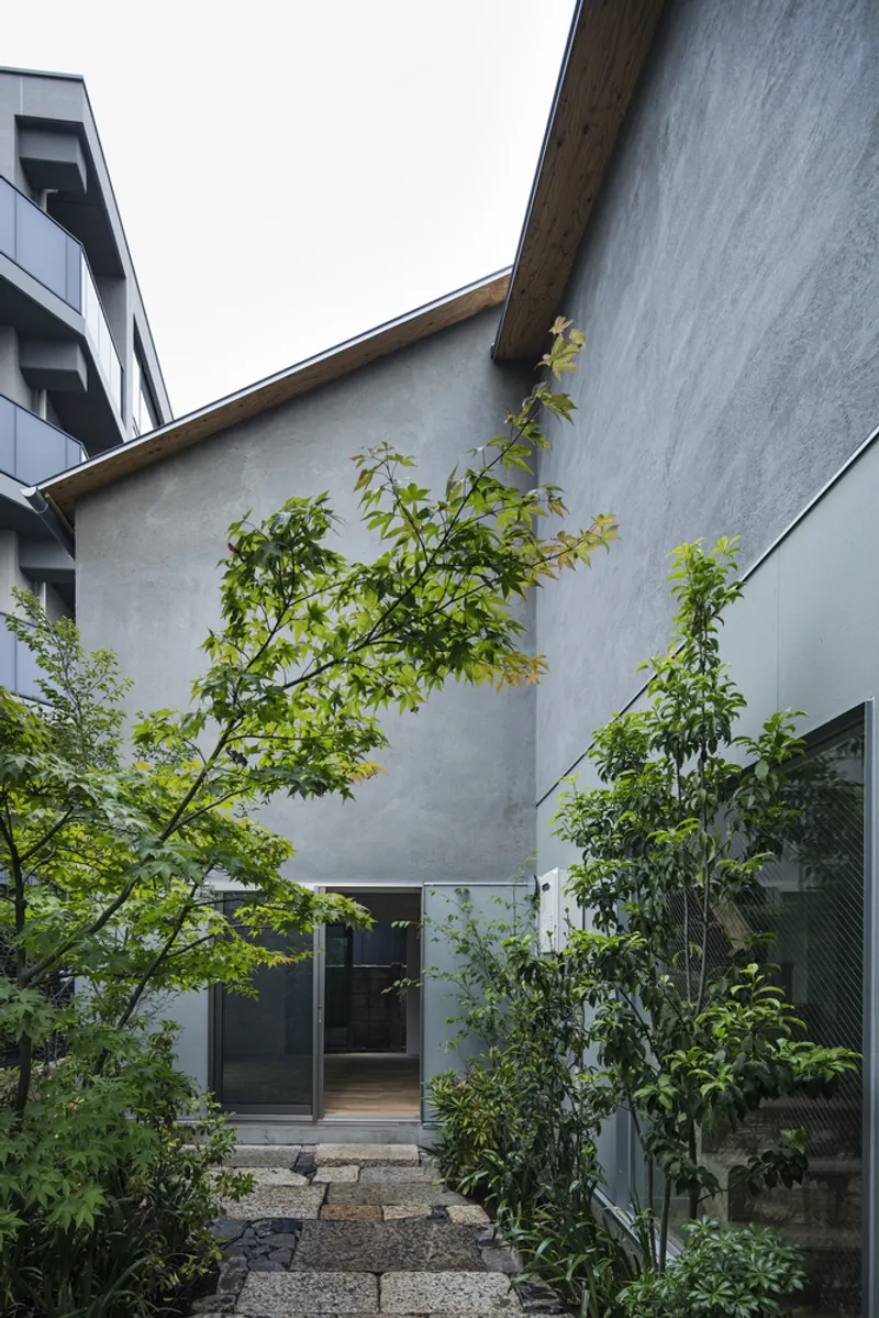 Smooth plaster facade with entrance door framed by young trees in a gravel courtyard
