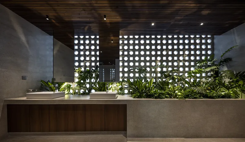 Bathroom vanity with twin basins behind perforated screen wall filtering daylight through planted beds